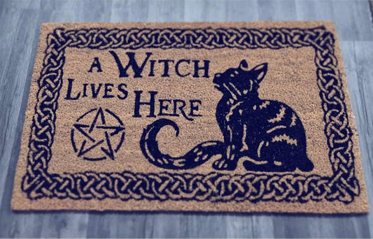 Photo of a doormat with a black cat and pentagram on along with the words 'A Witch Lives Here'