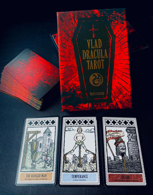 Photo of the Vlad Dracula tarot set with the guide box next to the set of cards and three cards laid out in front: The Hanged Man, Temperance and Death