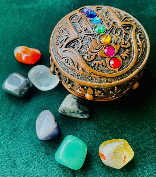 Photo of a round wooden box with an embossed palm on top and seven small gems running through it, next to chakra crystals.