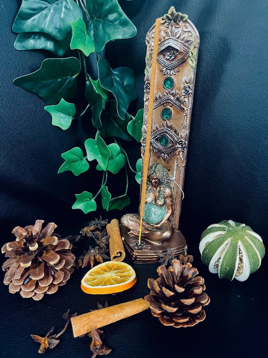 Photo of a vertical bronze Mother Earth incense burner next to leaves, pine cones and dried fruit.