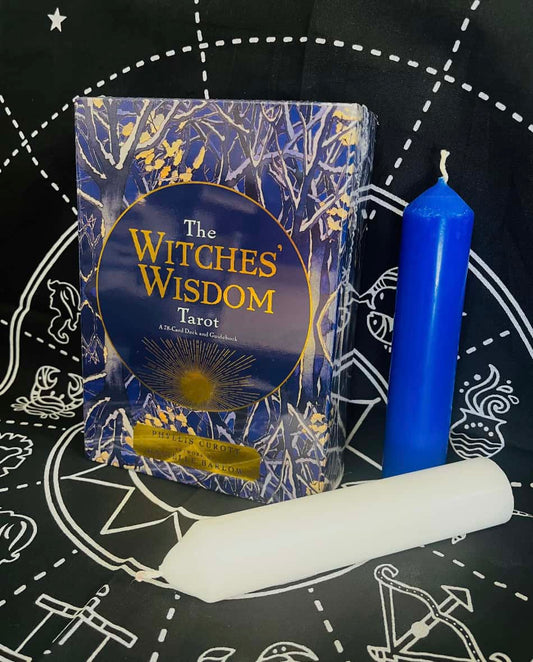 A picture with an altar cloth in the background and a box of The Witches' Wisdom tarot cards next to one blue and one white candle.