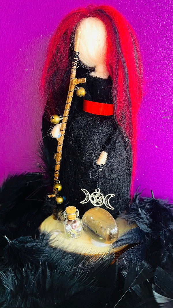 Photo of a handmade felt witch with red and purple hair and black robe with red sash..