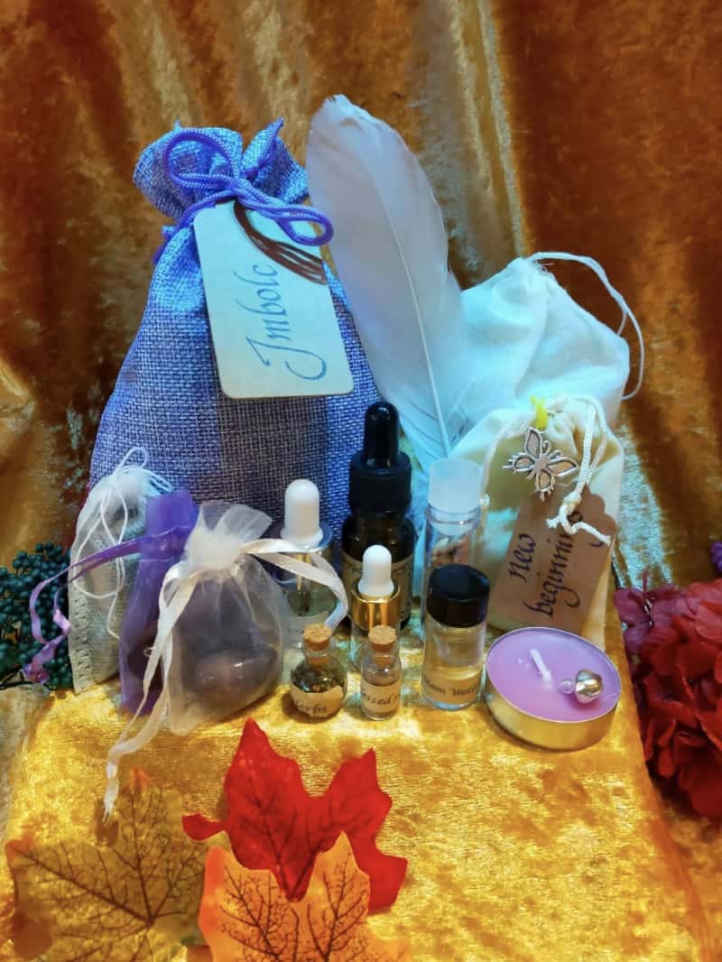 Photo of an imbolc spell bag and some of the contents, including amethyst, bell, jasmine incense, feather, blessed salts.