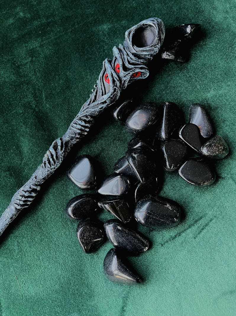 Photo is of a number of obsidian tumblestones next to a grey wand with red markings.