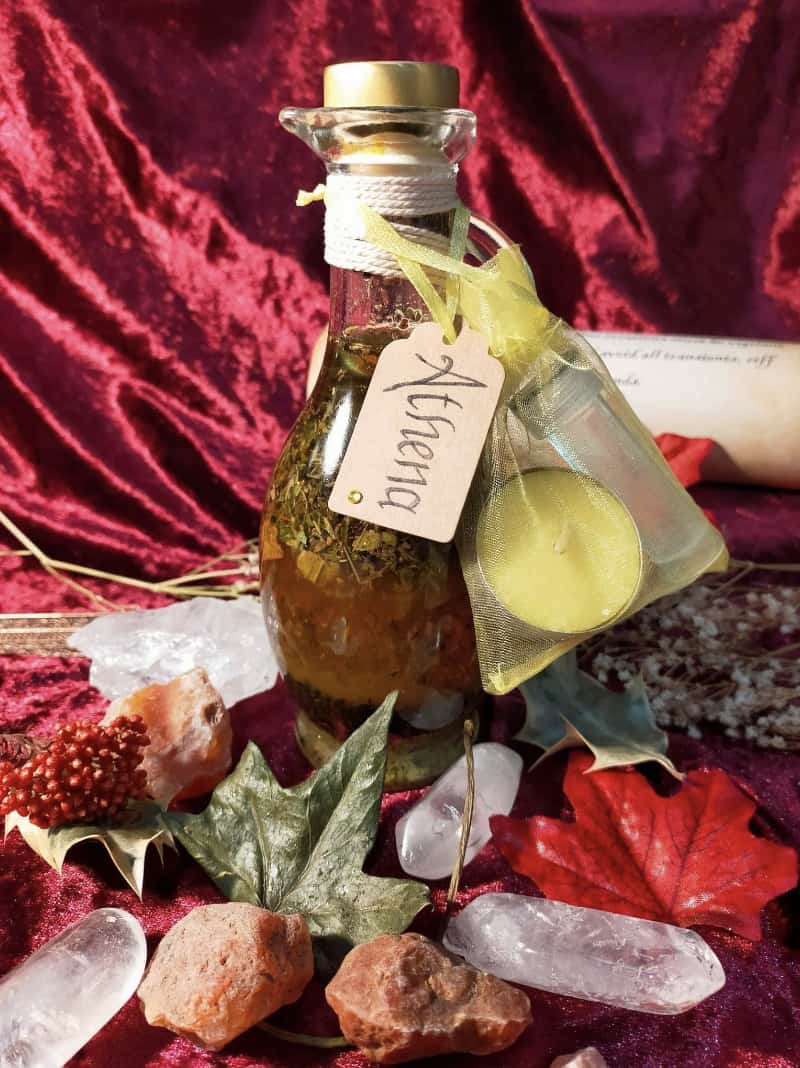 Image of a bottle of bath oil labelled Athena and containing herbs and flowers.