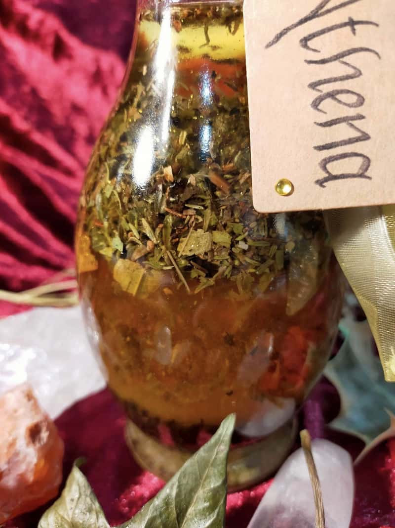 Image of a bottle of bath oil labelled Athena and containing herbs and flowers.