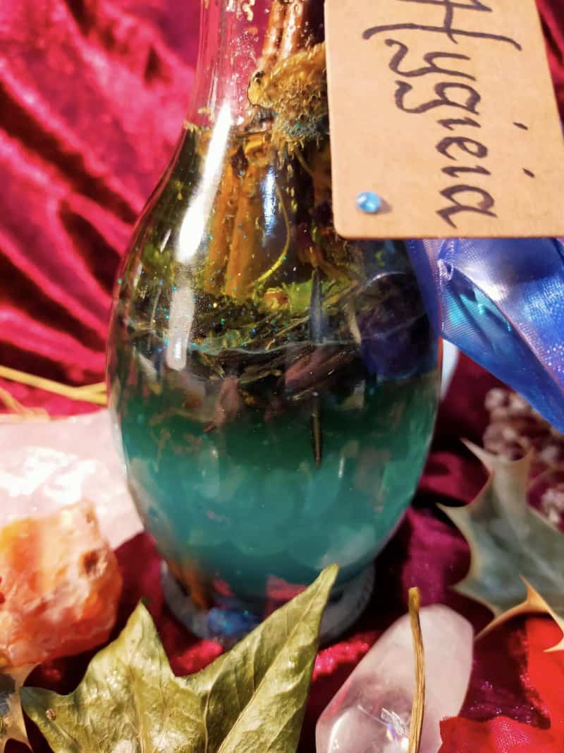 Image of a bottle of bath oil labelled Hygieia and containing herbs and flowers.