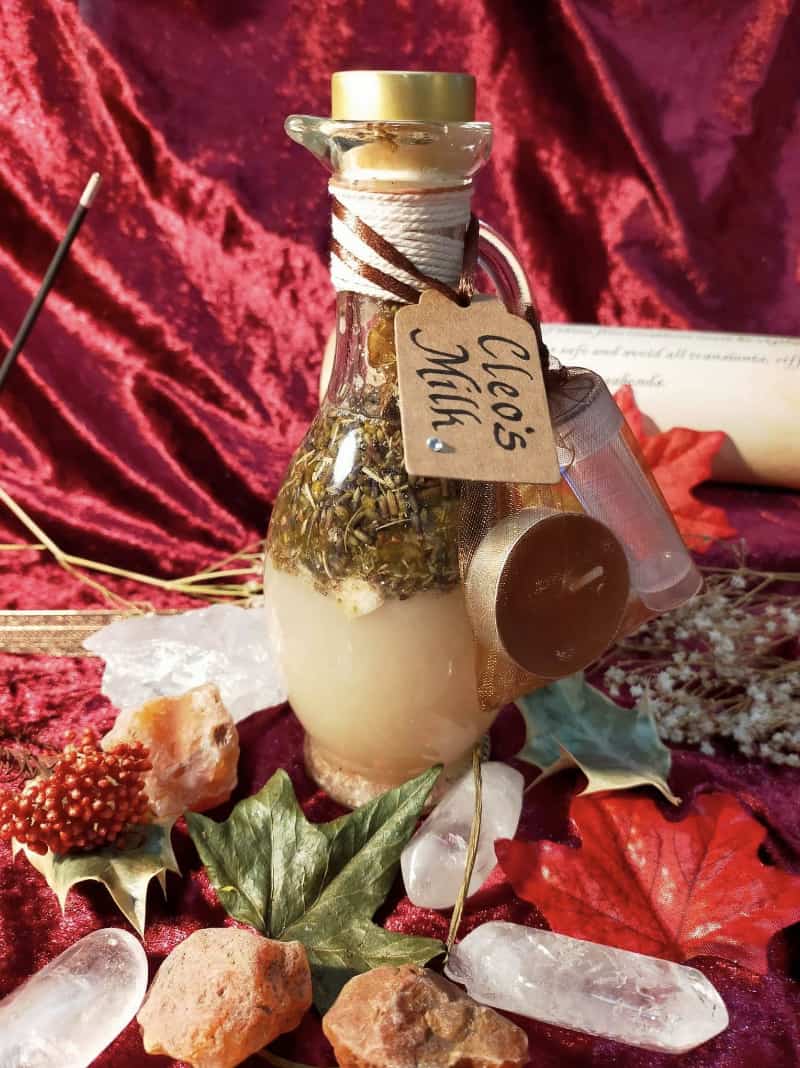 Image of a bottle of bath oil labelled Cleo's Milk and containing herbs and flowers.