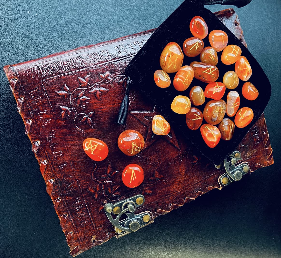 Photo of a set of carnelian crystal runes and black velvet pouch, resting on a leather journal.