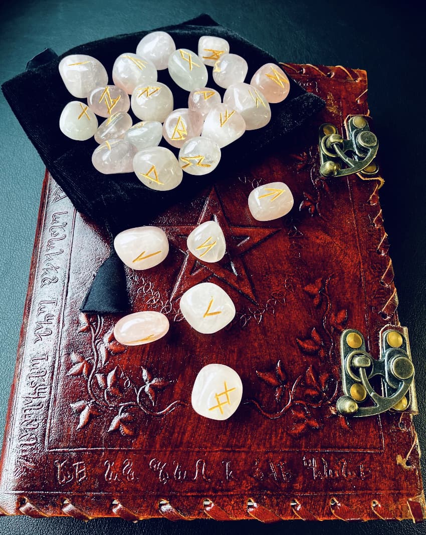 Photo of a set of rose quartz crystal runes and black velvet pouch, resting on a leather journal.