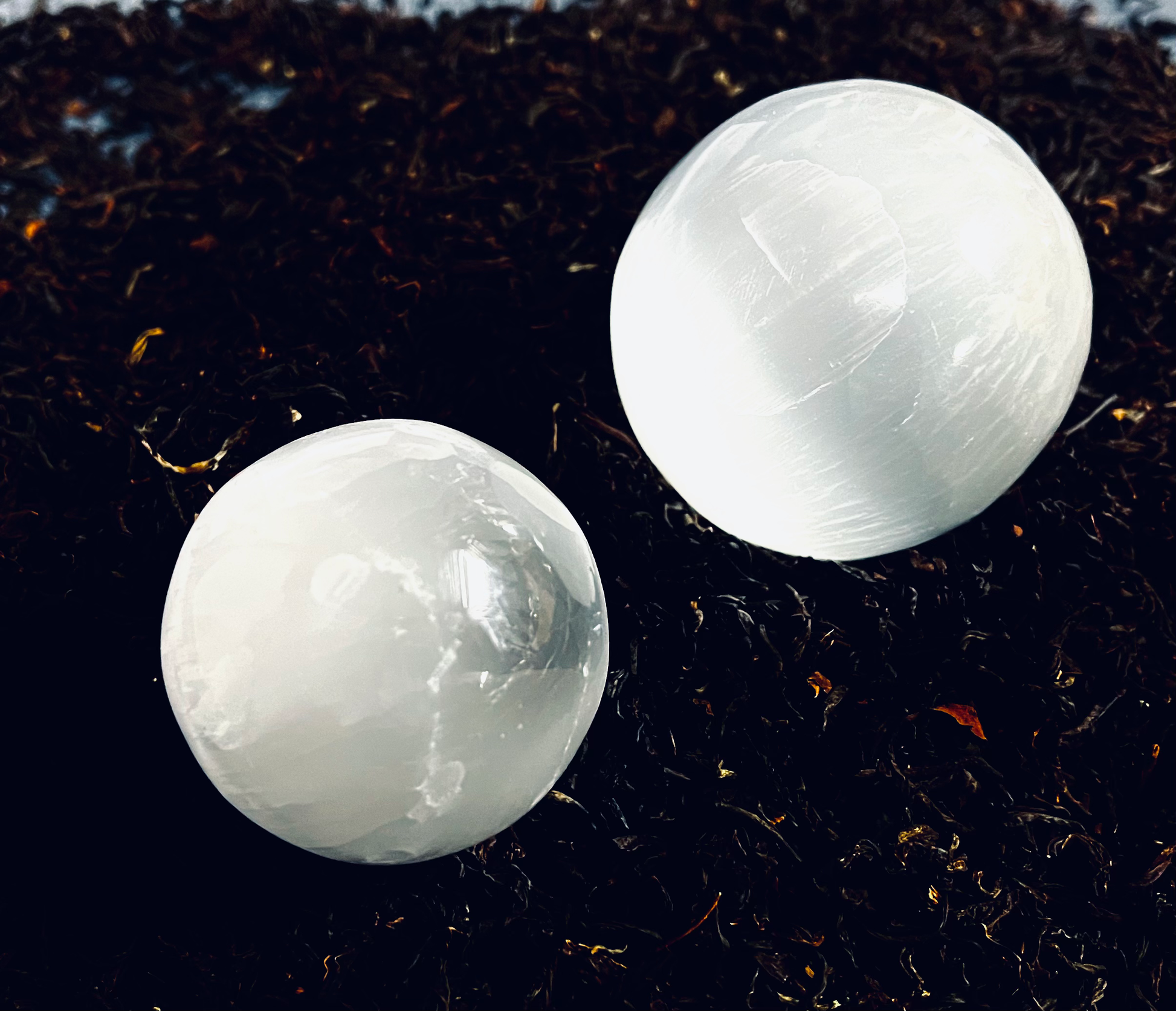 Photo of two selenite orbs on a bed of dried flowers and herbs.