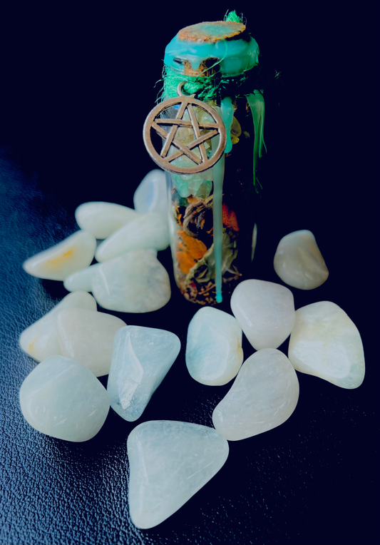 Photo of several garnierite tumblestones next to a small spell bottle sealed with green wax.