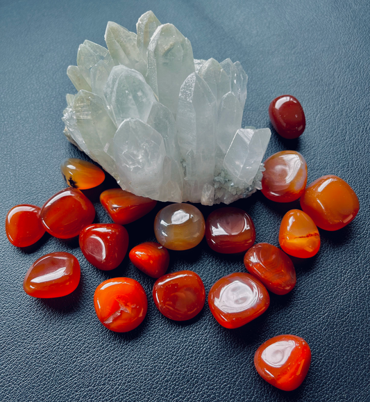 Photo of a number of carnelian tumblestones scattered around a large piece of quartz.