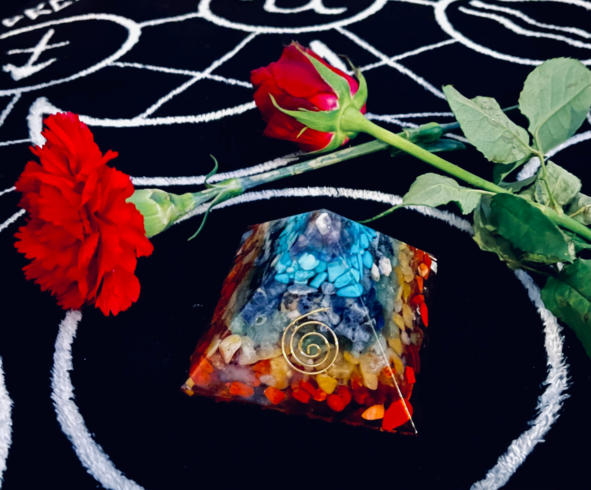 Photo of a resin chakra pyramid sitting on a black and white altar cloth. Two red carnations are behind the pyramid.