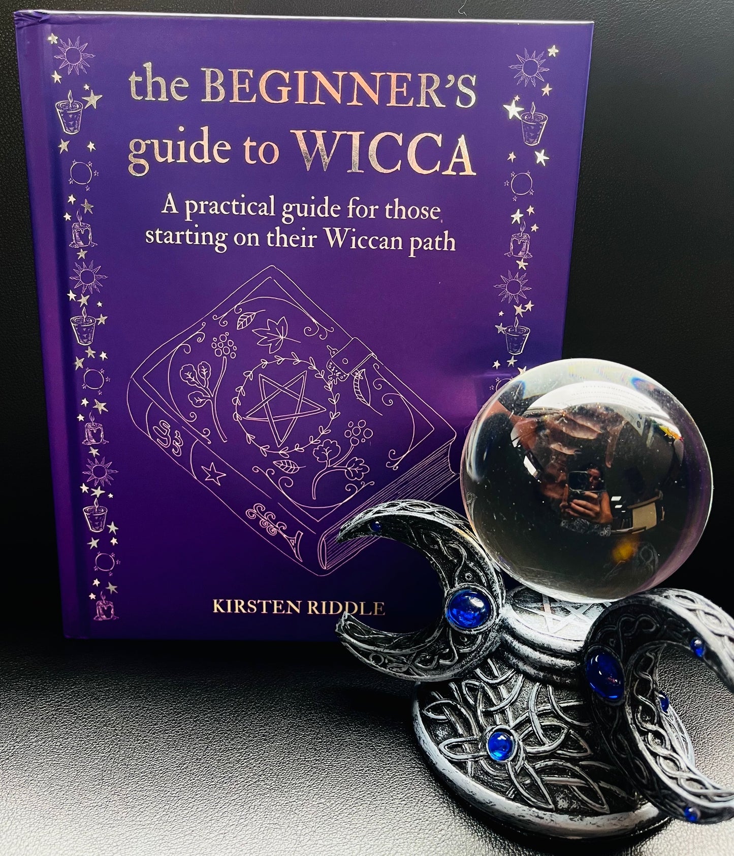 Image of the book The Beginners Guide to Wicca with a crystal ball and stand to the side.