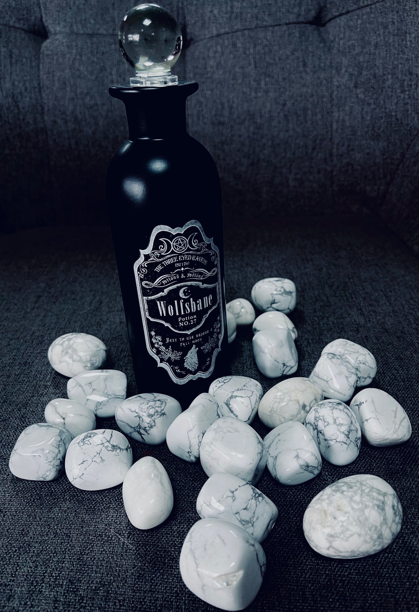 Photo of several large howlite tumblestones next to a back bottle reading Wolfsbane