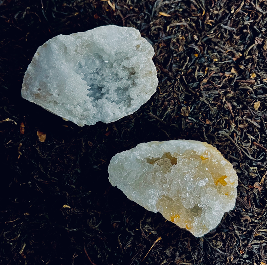 Photo of two quartz geodes, one with hints of blue, one with tints of orange, on a bed of dried flowers and herbs