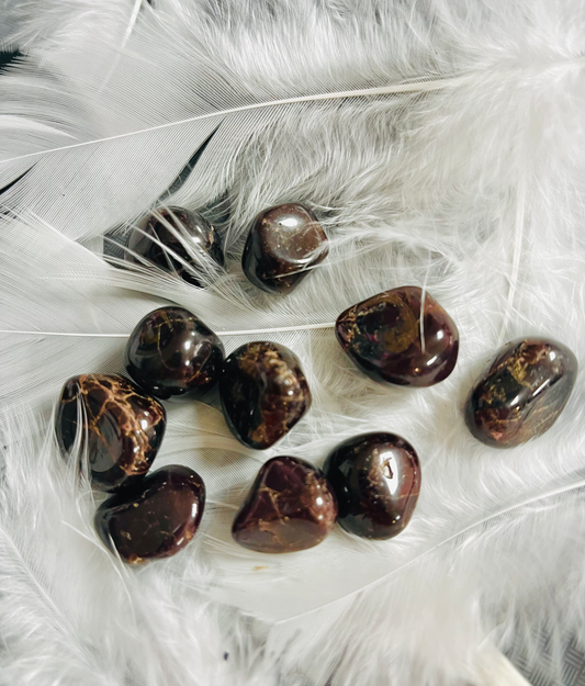 Photo of a number of small garnet tumblestones sitting atop some white feathers.